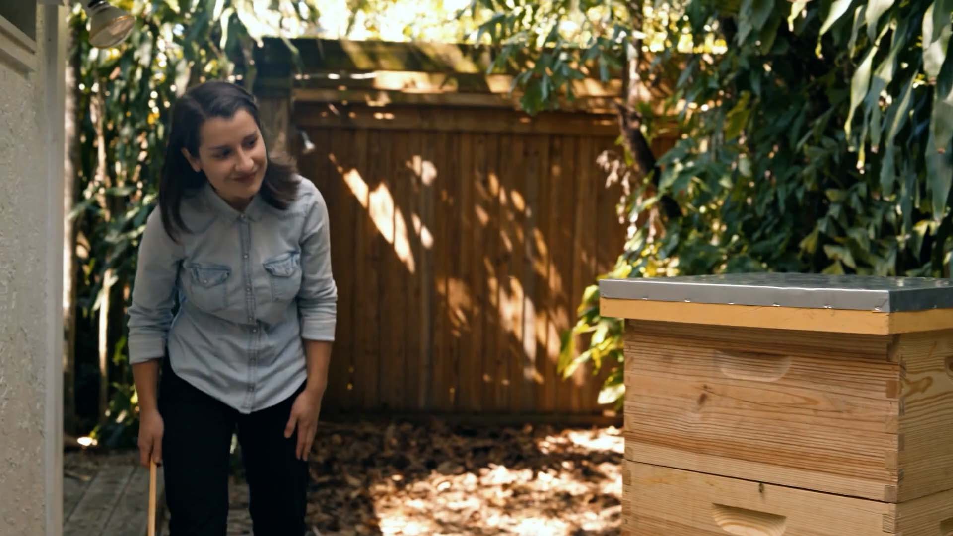 A beekeeper stands beside a beehive