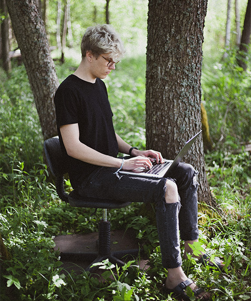 A person in a forest sits in an office chair, typing on a laptop. health benefits of nature