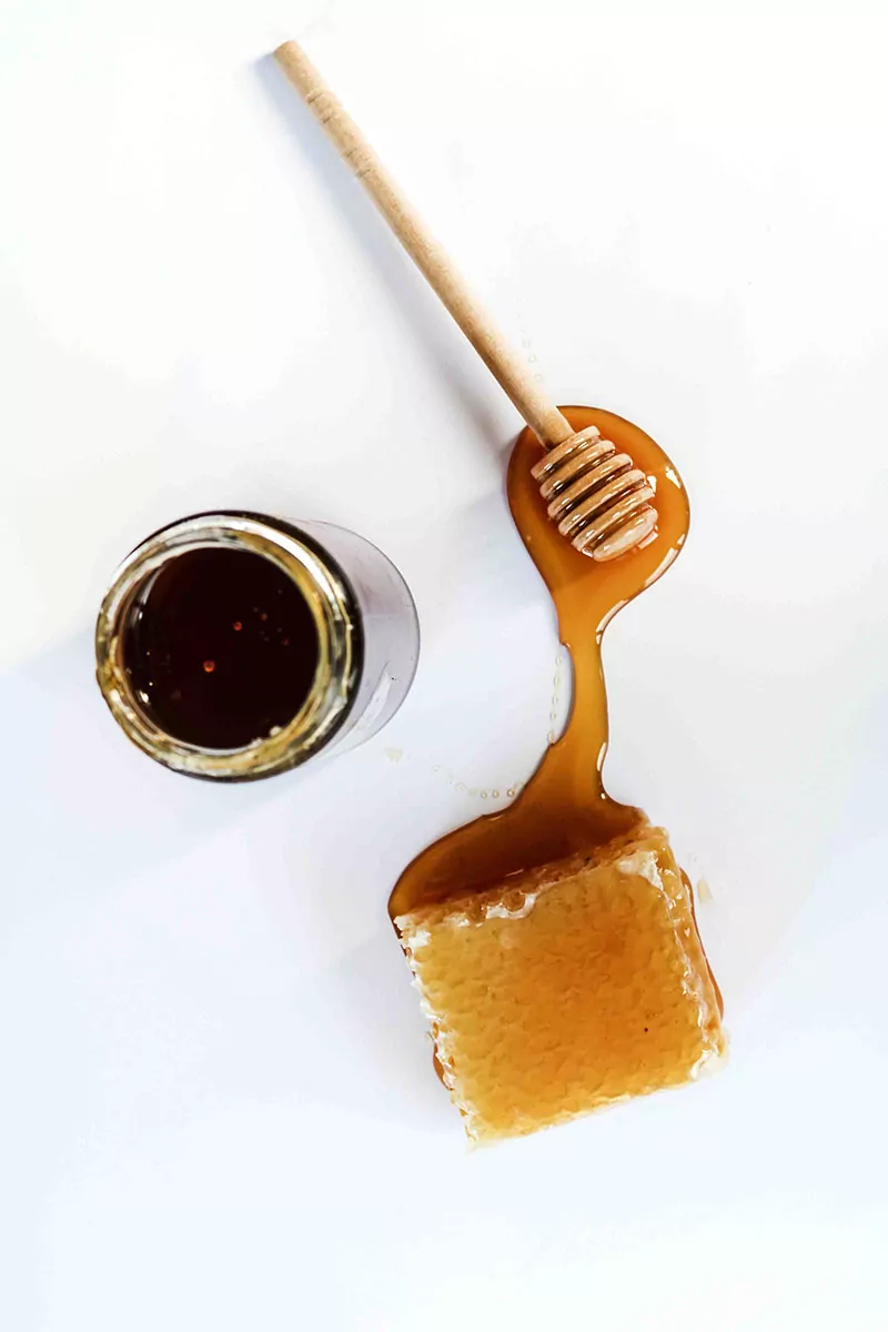 A jar of honey beside a cube of honey comb. honey bee hive products